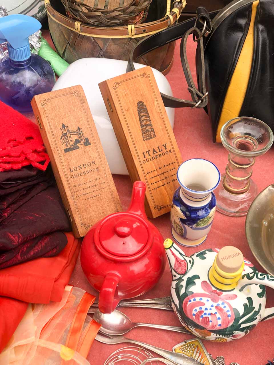 Vintage market table with a red teapot, ceramic jugs, and wooden guidebooks for London and Italy