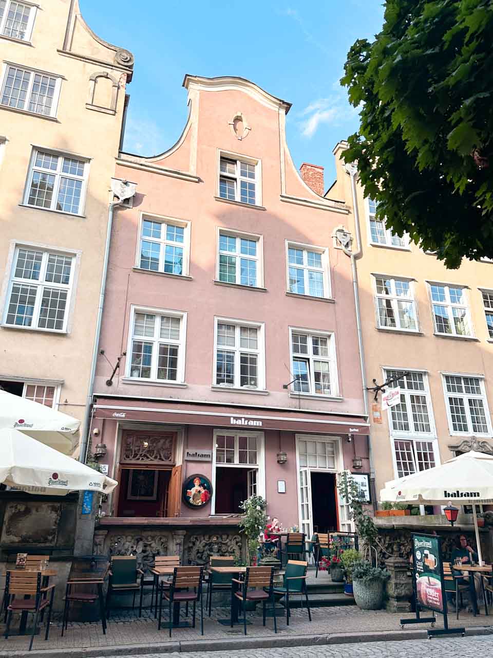 Outdoor seating at Balsam restaurant on Piwna Street in Gdańsk, in front of a pastel pink townhouse