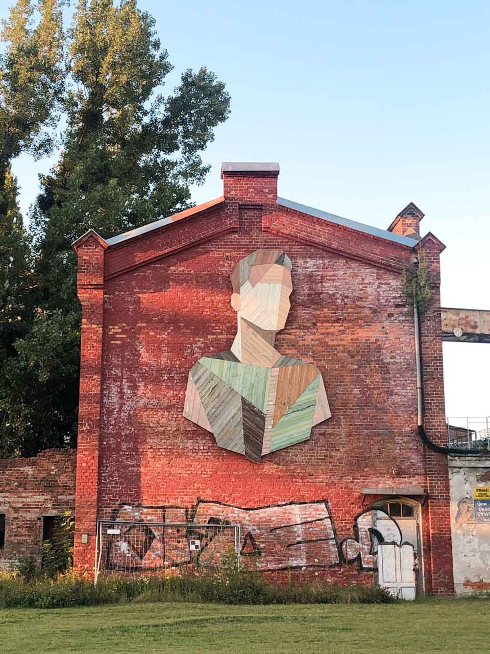 Large mural made of wood panels on a red brick wall of an old building in Gdańsk