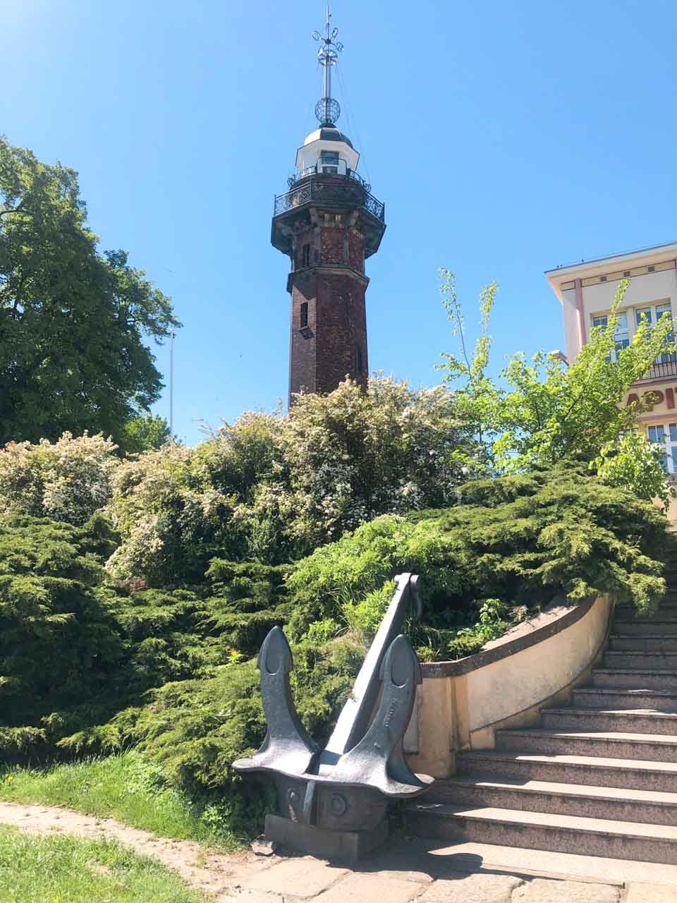 Historic red brick water tower in Nowy Port, with a large anchor displayed near the entrance steps