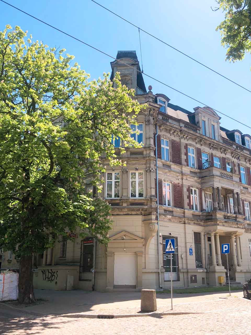 Ornate corner building in Gdańsk’s Nowy Port district, partly shaded by a leafy tree