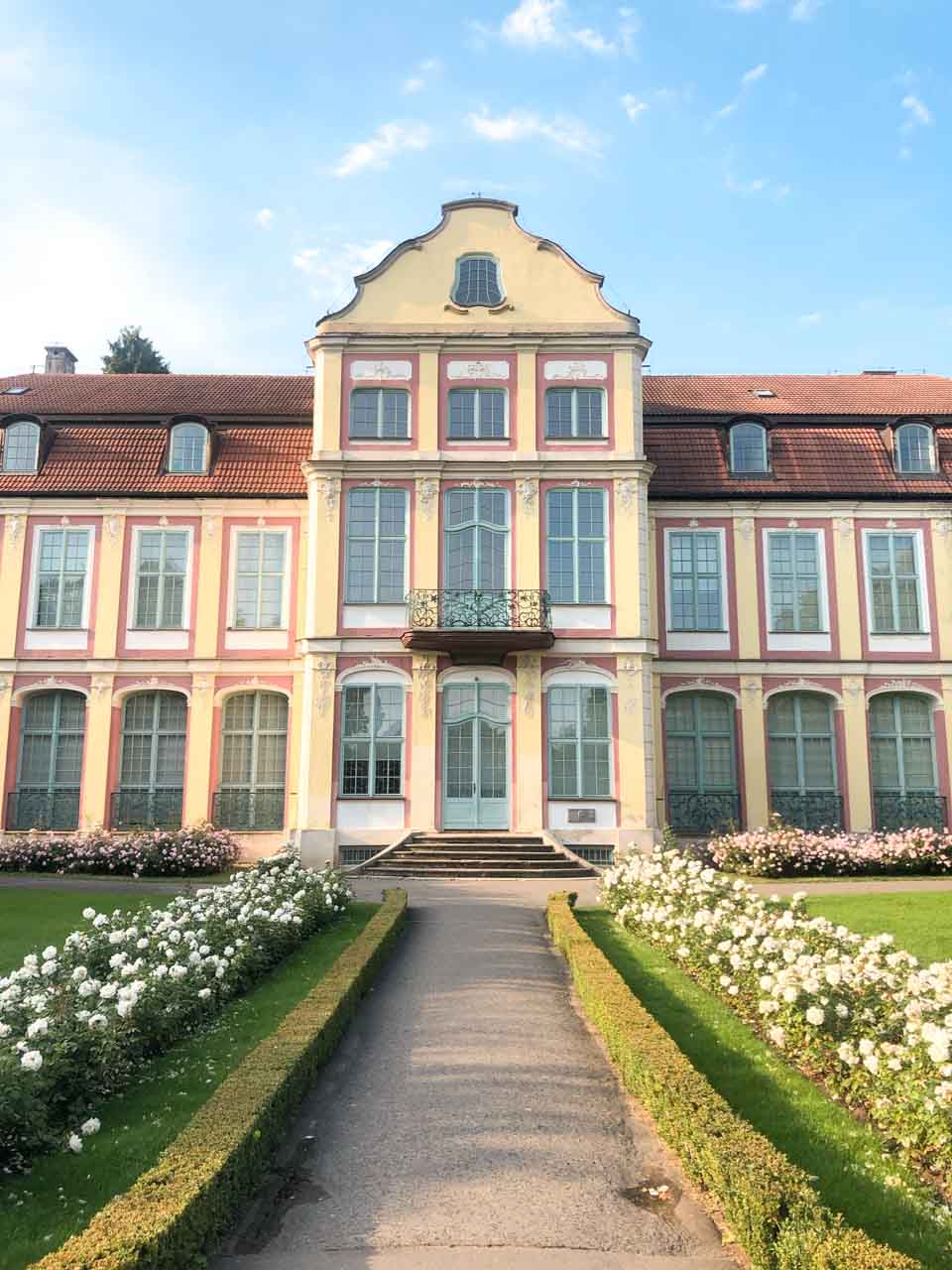 The elegant front of the Abbots' Palace in Oliwa, framed by white roses and manicured hedges