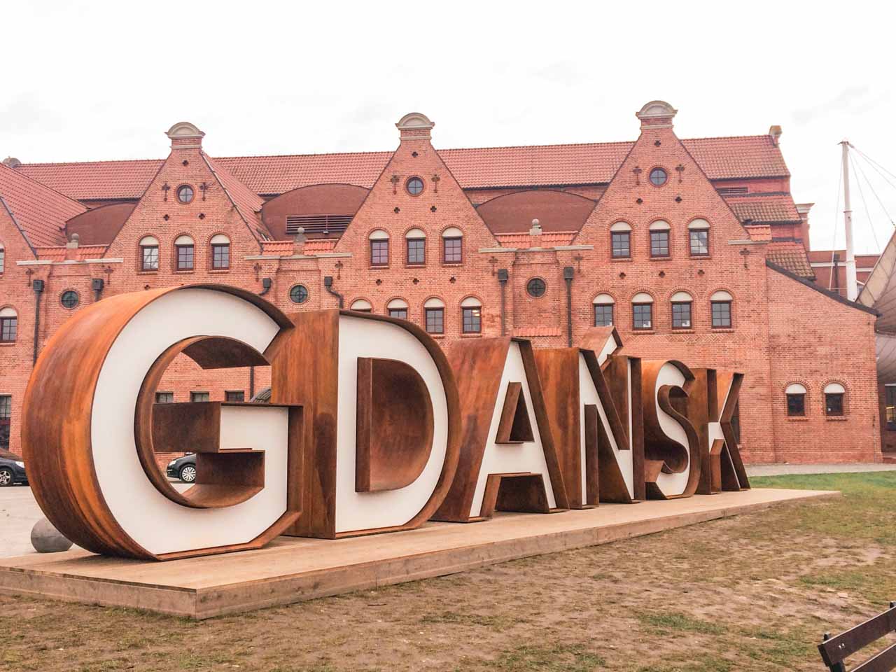 Large GDANSK sign made of rusted steel and white letters, with the Polish Baltic Philharmonic building in the background