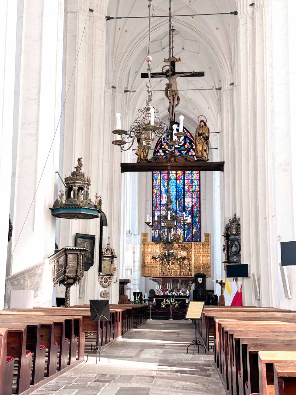 Interior of St. Mary’s Church in Gdańsk, with wooden pews, a golden altar, and colourful stained glass