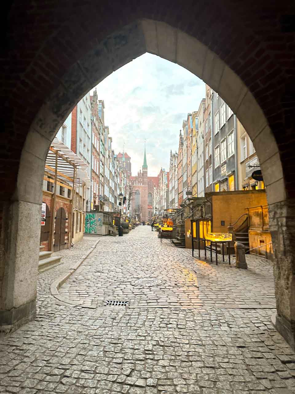 Mariacka Street viewed through a brick archway, lined with amber shops and cobblestones
