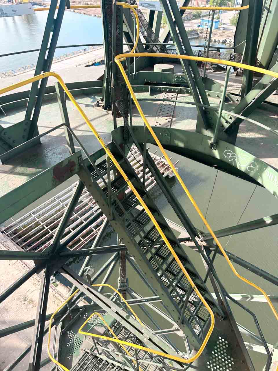 Looking down the industrial stairs of a shipyard crane in Gdańsk, with yellow railings and a view of the water