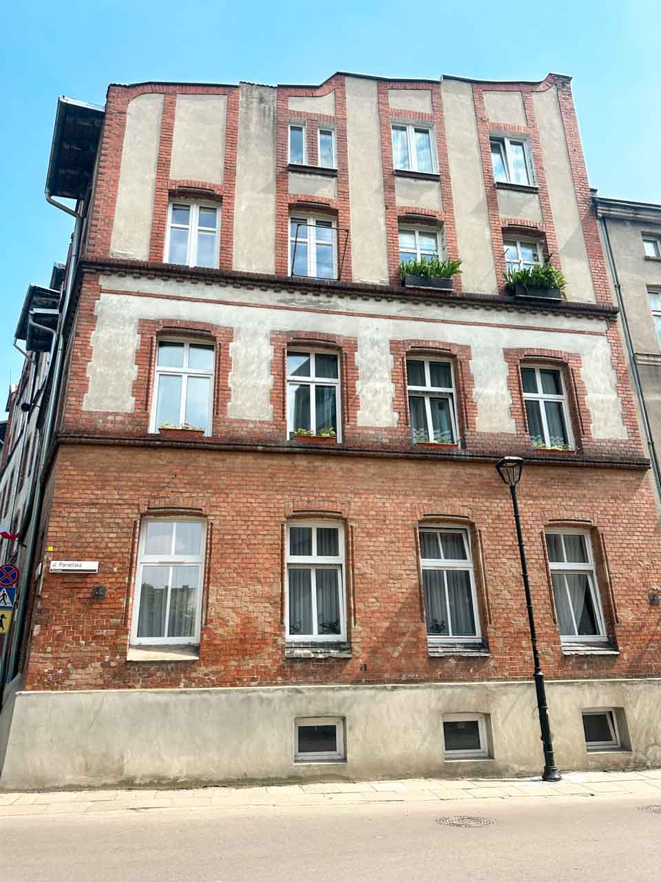 Red brick residential building in the Dolne Miasto district with white-framed windows and potted plants