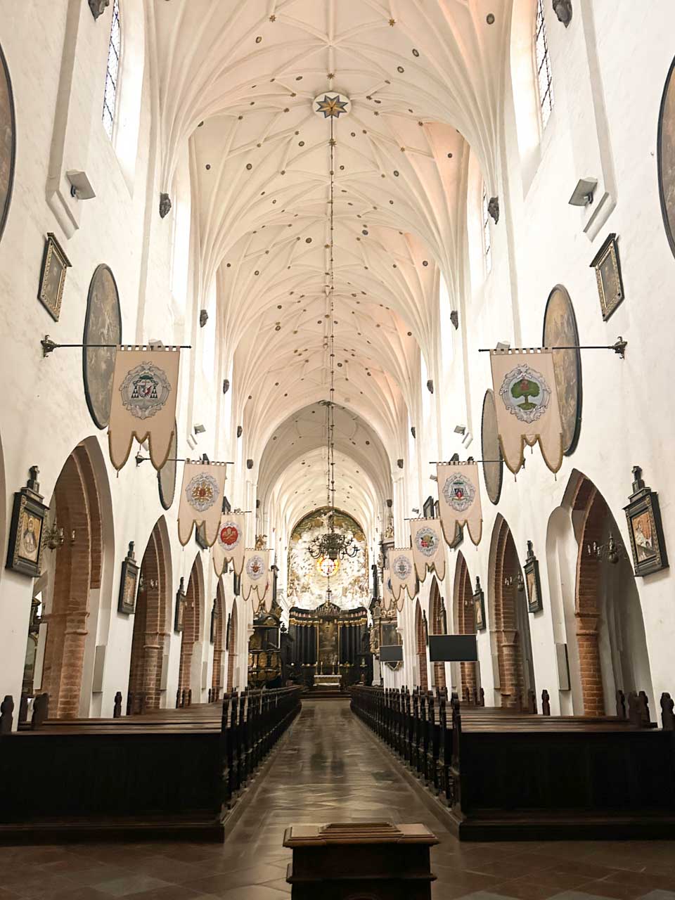 Interior of the Oliwa Cathedral with vaulted ceilings, heraldic flags, and a view down the nave to the altar