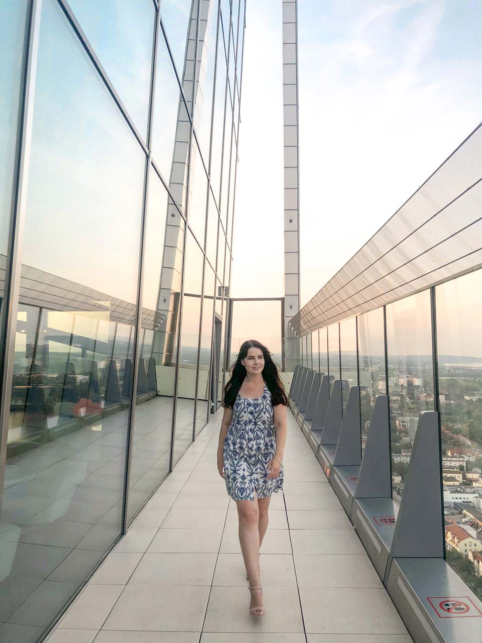 Woman walking along the glass terrace of Olivia Star in Gdańsk, with panoramic city views in the background