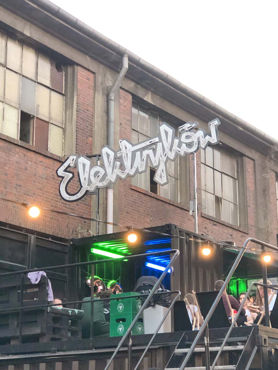 Outdoor seating on Elektryków Street in Gdańsk, with a glowing neon sign and colourful lights under a shipping container roof