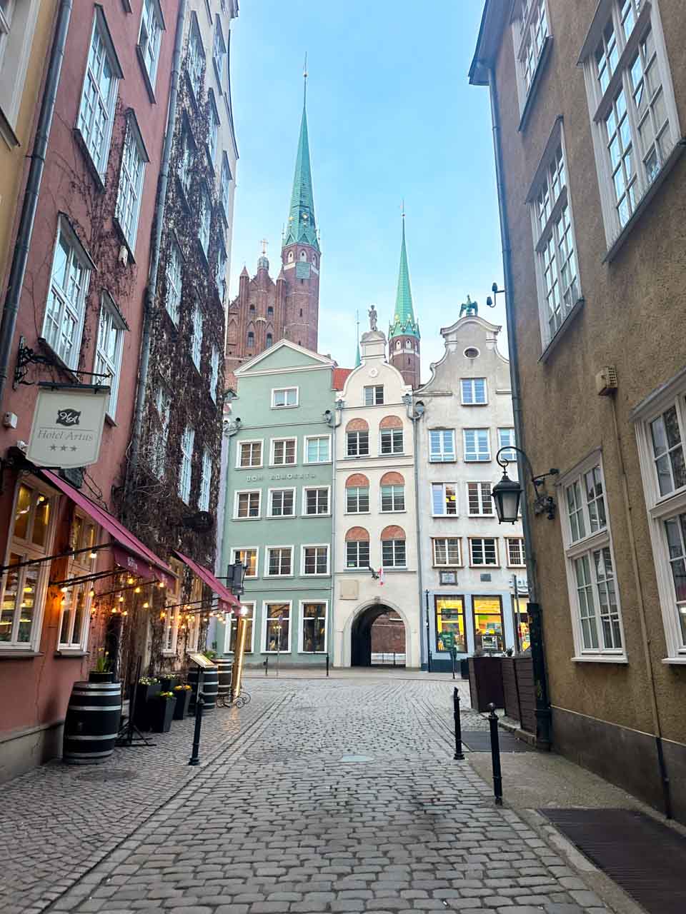 Quiet cobbled street in Gdańsk’s Main City, with pastel buildings and the spires of St. Mary’s Church in the distance