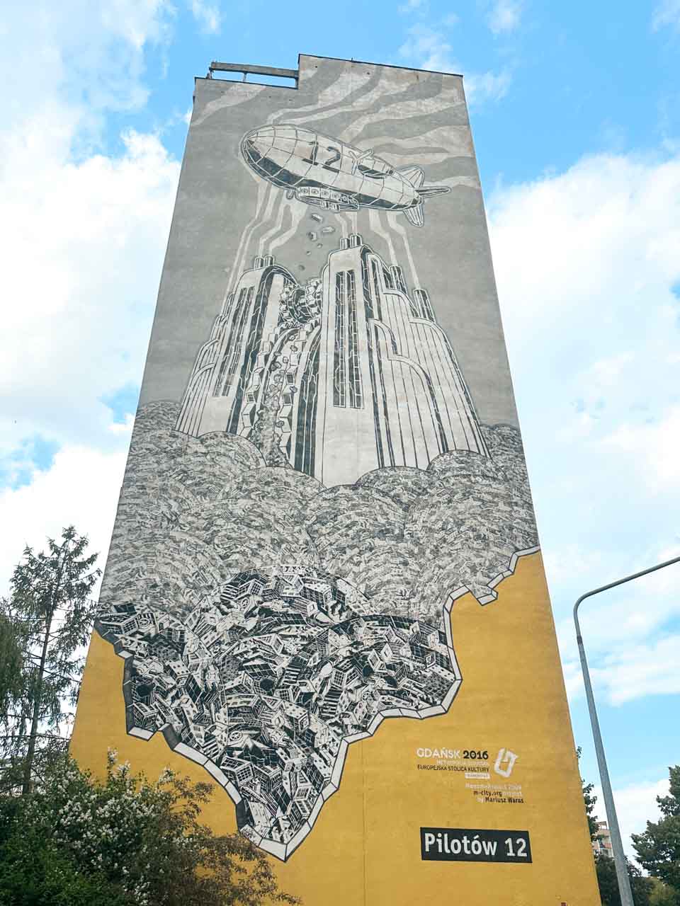 Tall mural of a zeppelin flying over a futuristic city, surrounded by tiny black-and-white buildings