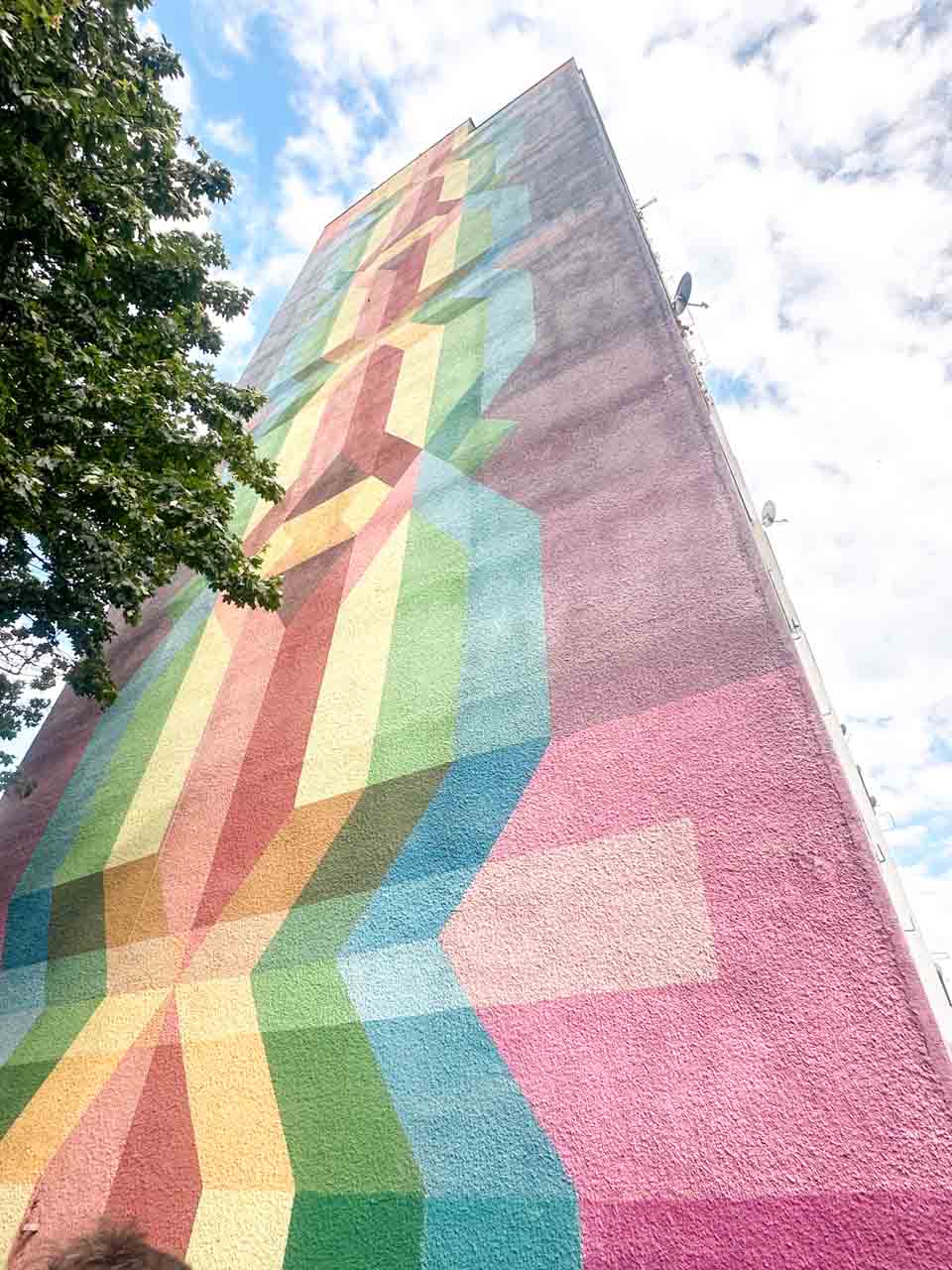 Vibrant mural with overlapping rainbow-coloured geometric patterns climbing up the building wall