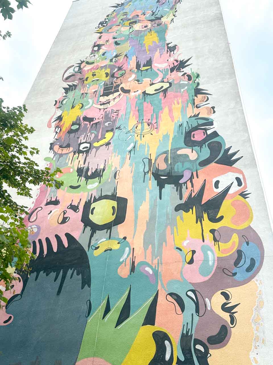 Tall mural in Gdańsk’s Zaspa showing colourful cartoon-like faces and eyes melting into each other on a grey high-rise wall
