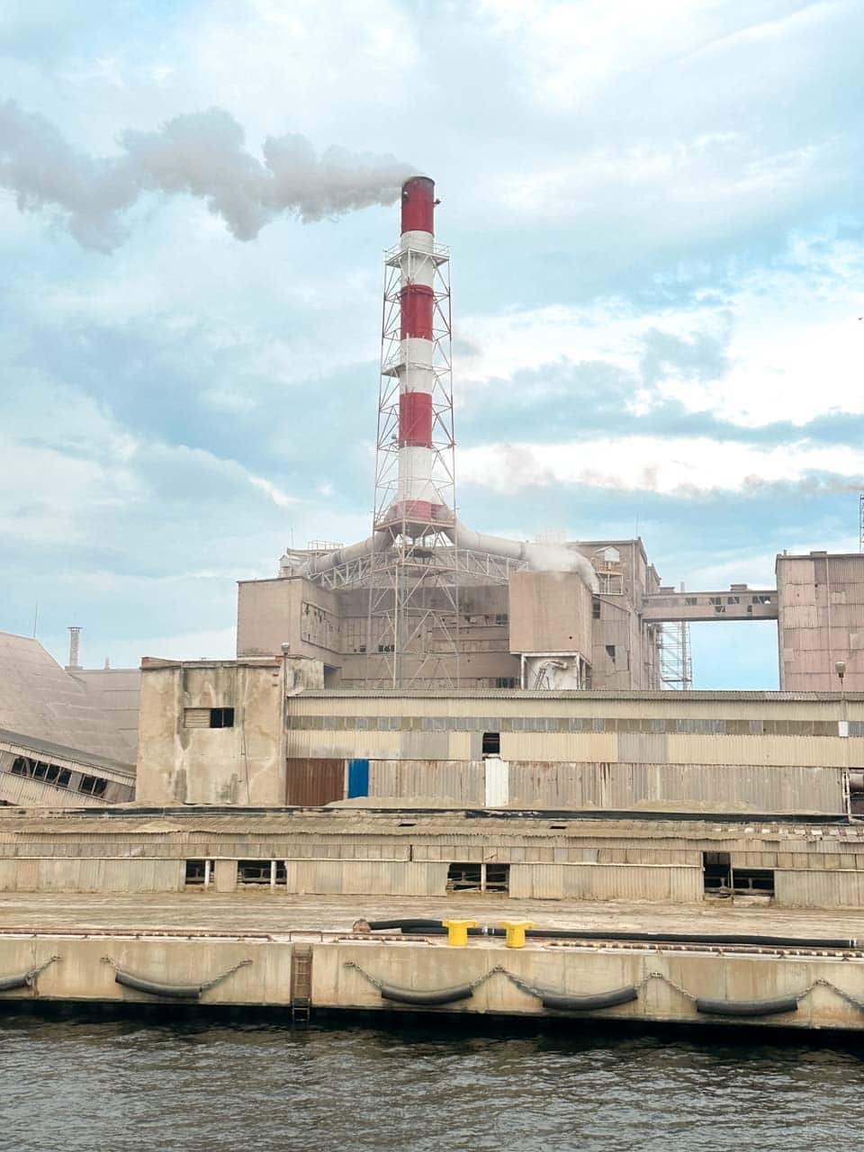 Large industrial plant in Gdańsk with a red and white chimney releasing thick white smoke