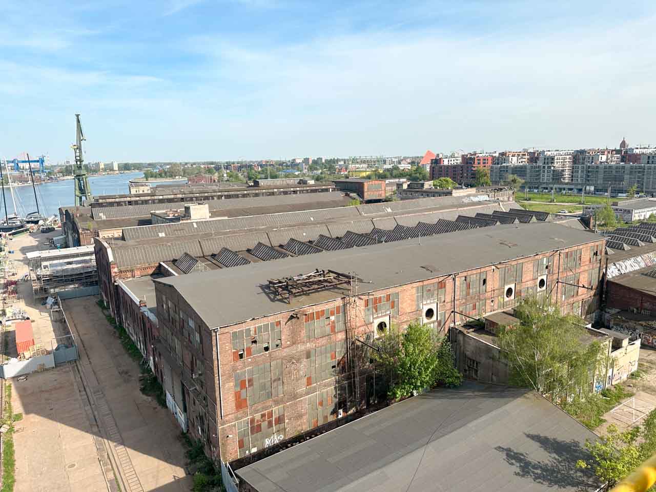 Aerial view of large brick warehouses in the Gdańsk shipyard, with the river and city in the background