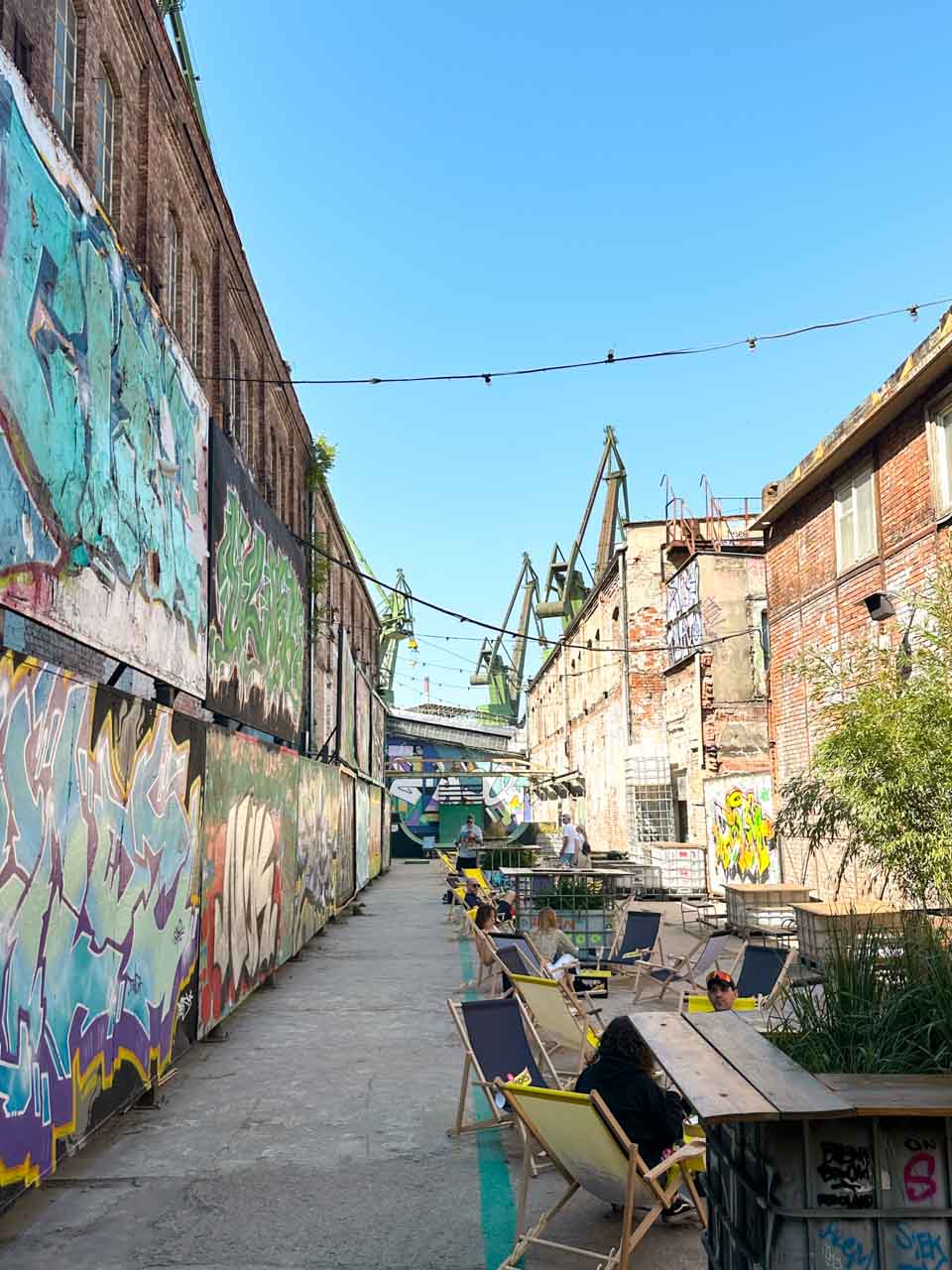 Outdoor seating area with deck chairs and street art in a narrow alley of 100cznia in Gdańsk