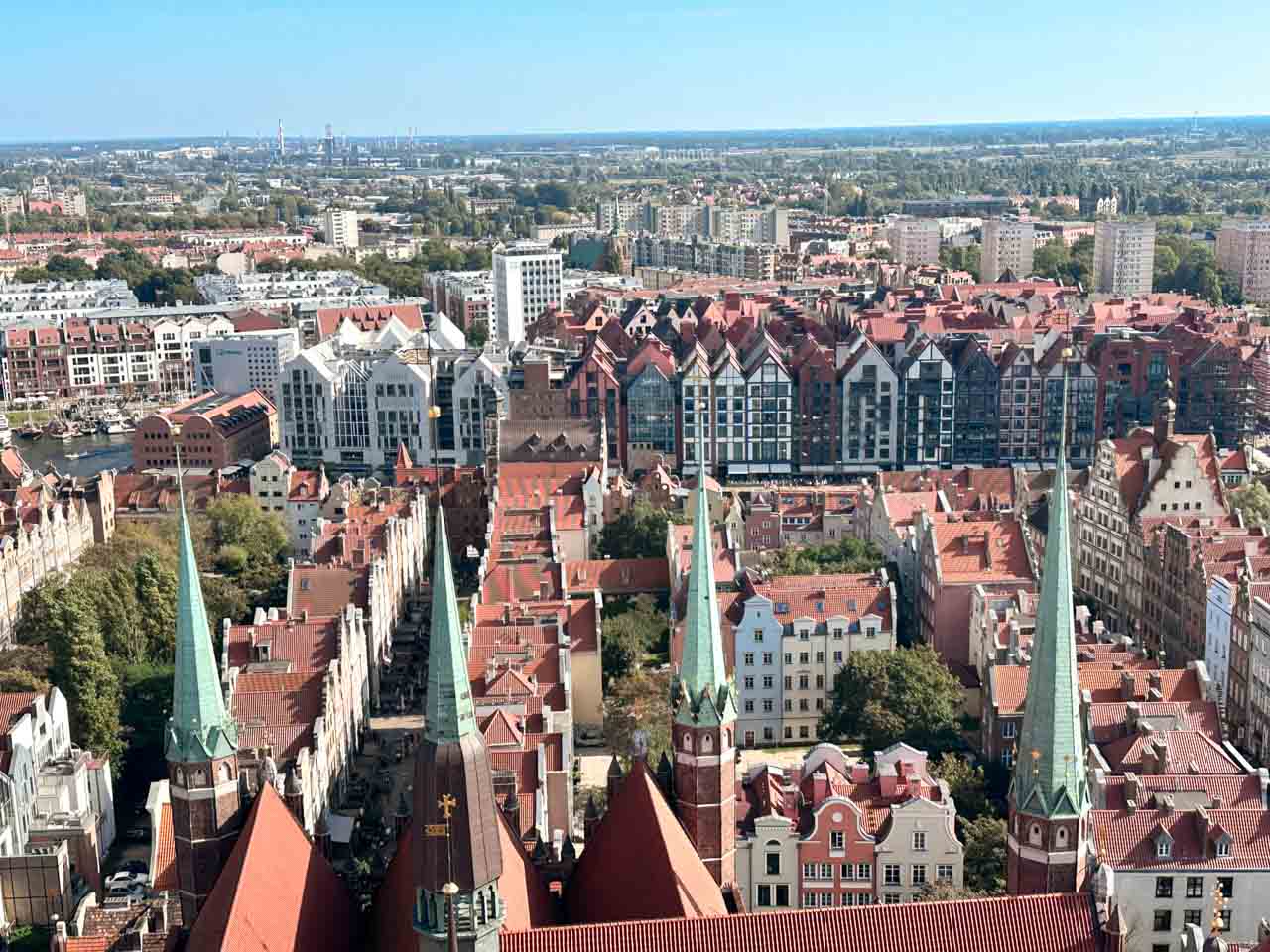 Aerial shot of Gdańsk's Main City with green spires, narrow streets, and modern buildings in the back