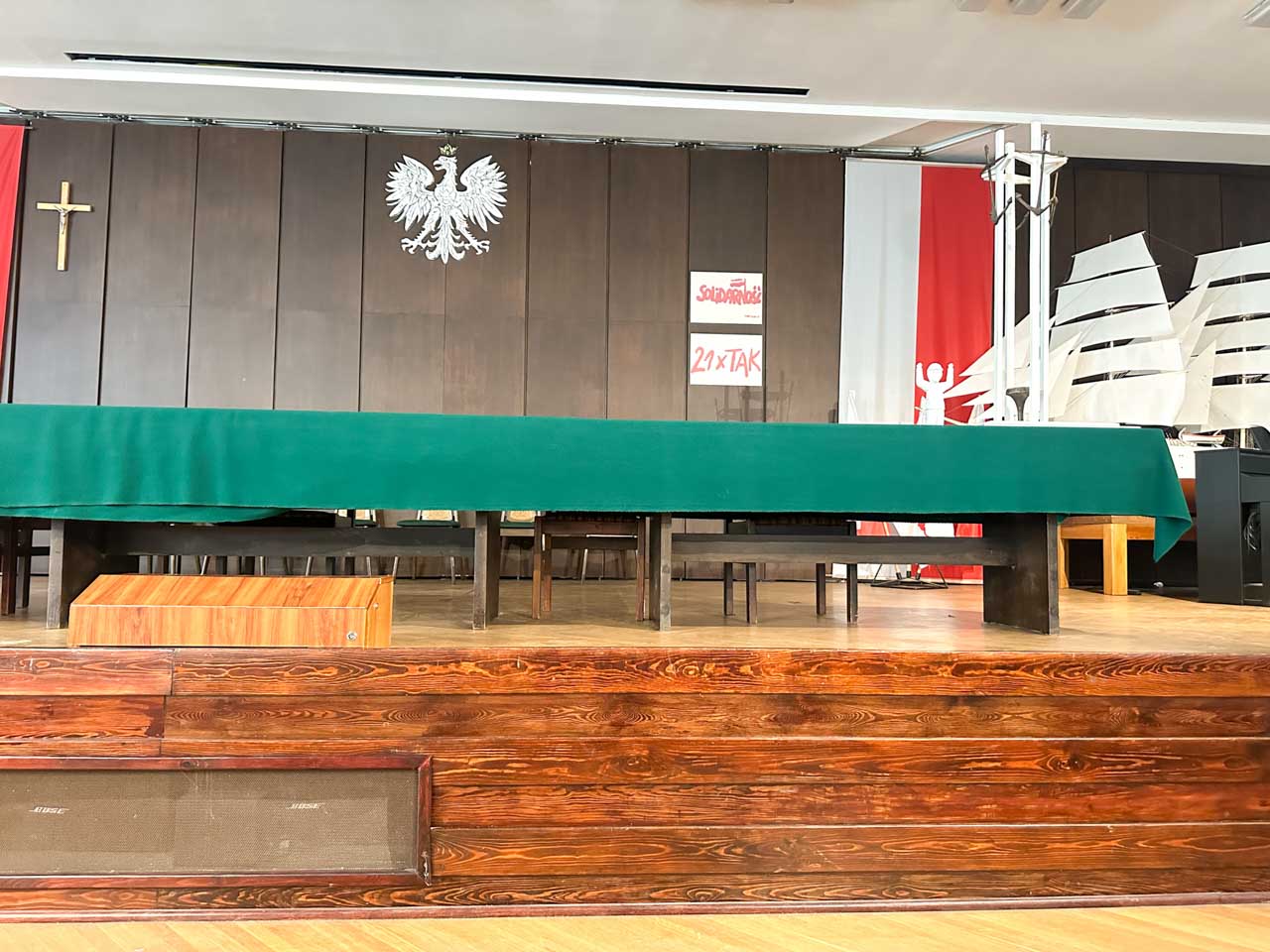 Close-up of the stage in the BHP Hall with a green tablecloth, Polish flag, and Solidarity signs