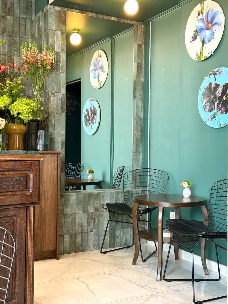 A cosy corner at Laba, a flower shop and specialty coffee spot, with dark green walls, fresh flowers, and circular floral wall art