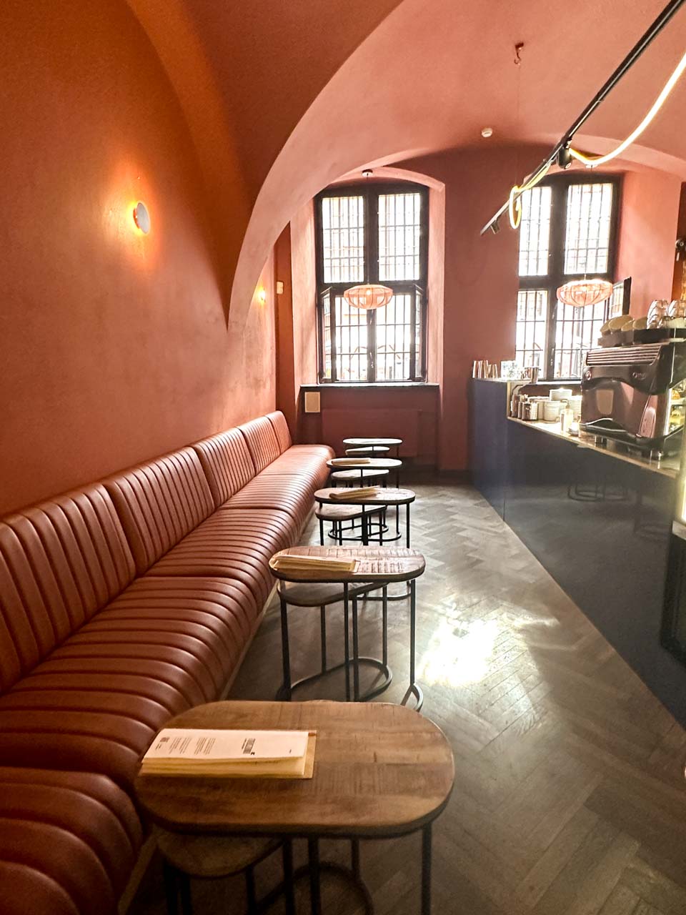 The interior of Ratuszowa Caffe Cocktails with terracotta-coloured walls, arched ceilings, and a long leather bench with small round tables