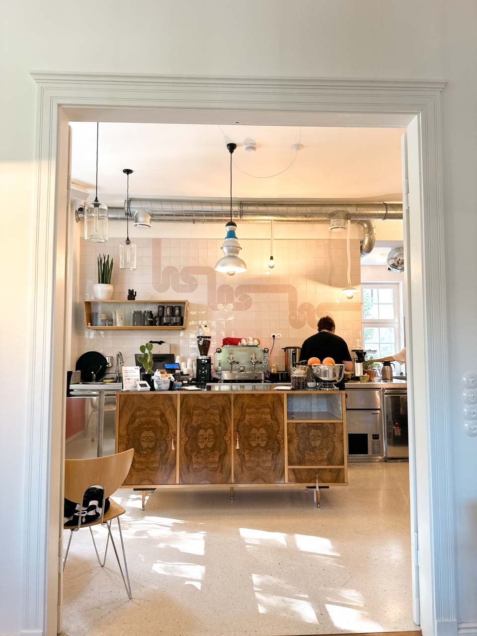 A look into the café’s open kitchen area, with a barista at work behind a wooden counter and soft light coming through the windows