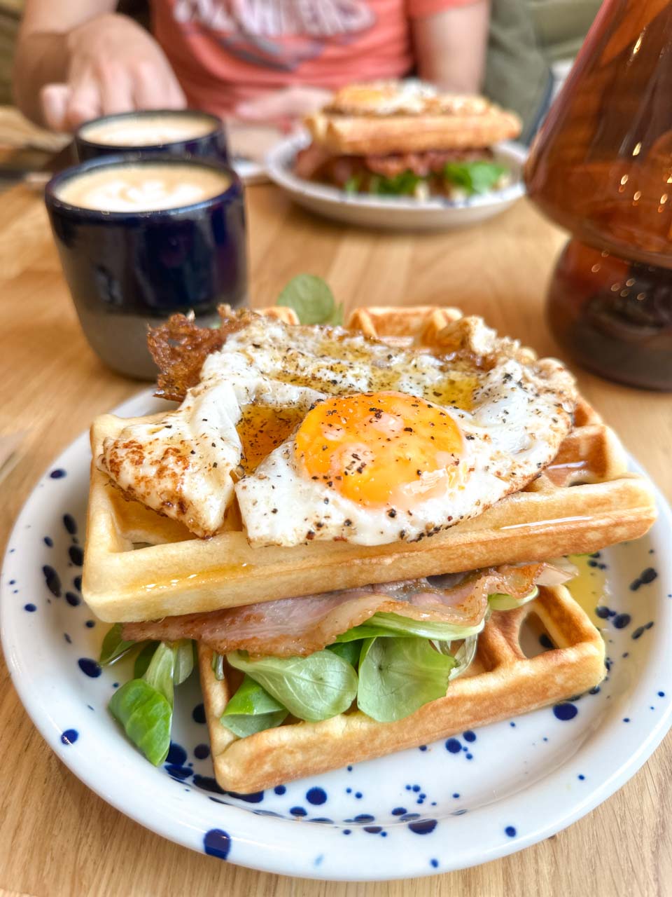 Stacked waffles with lettuce, bacon, and a sunny-side-up egg on top, served with coffee at Doppio Club Cafe in Gdańsk