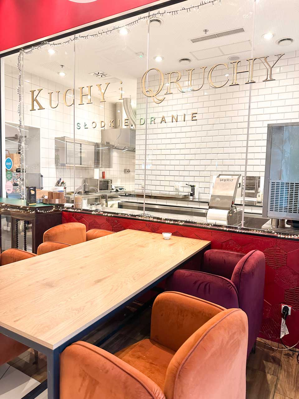 Seating area at Kuchy i Qruchy café with orange and purple velvet chairs and an open kitchen behind glass