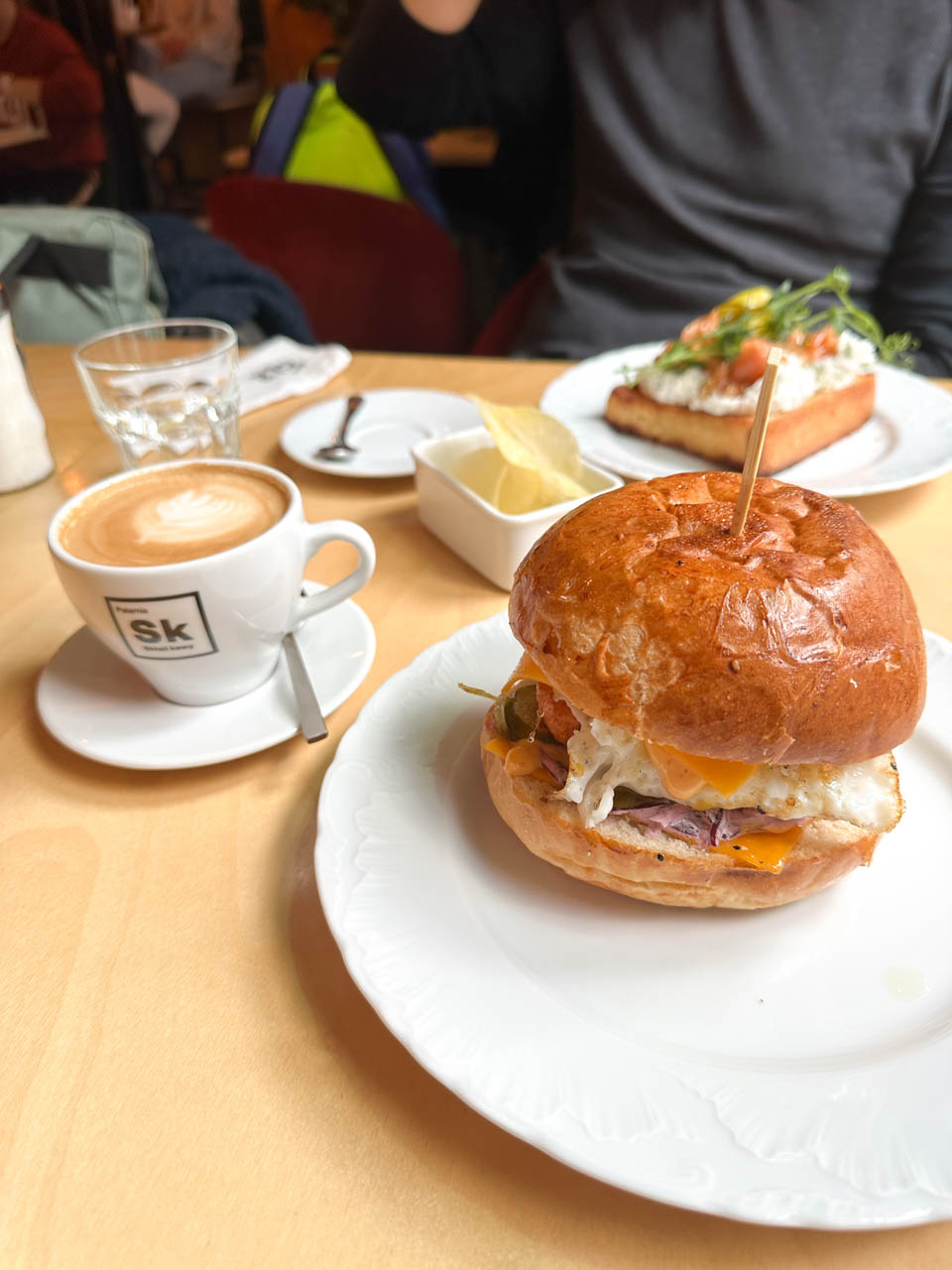 A toasted breakfast bun with egg and melted cheese served at Pomelo Bistro in Gdańsk, alongside a flat white and a dish of crisps