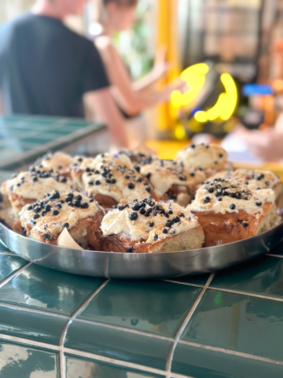 A tray of frosted buns topped with crumble and blueberries at Łąka Bar in Gdańsk, set on a tiled green counter