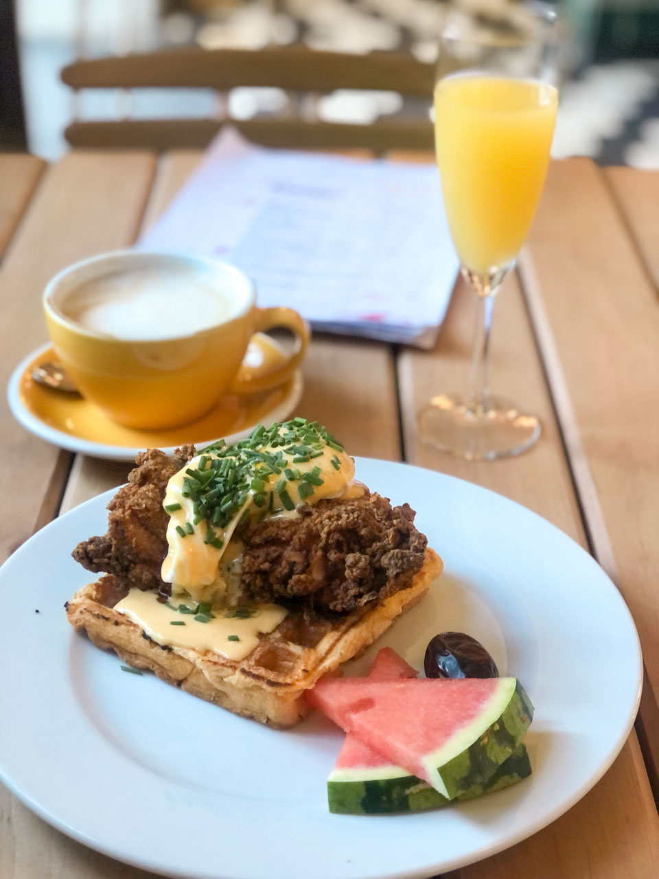 A serving of chicken and waffles with hollandaise sauce, watermelon slices, and a mimosa at Łąka Bar in Gdańsk