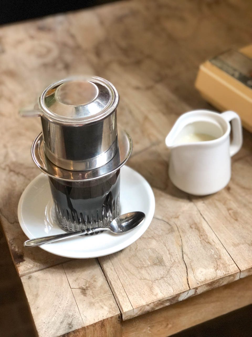 A Vietnamese-style drip coffee set with a small jug of condensed milk on a rustic wooden table at Łąka Bar in Gdańsk