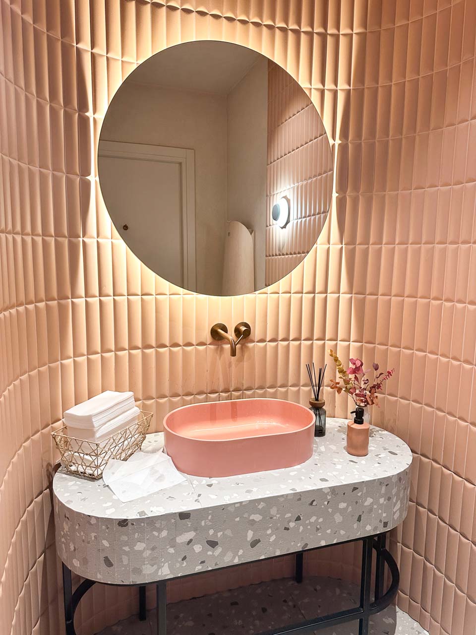 A modern bathroom at Mimosa in Gdańsk with a terrazzo sink, pink tiled walls, and a glowing round mirror above