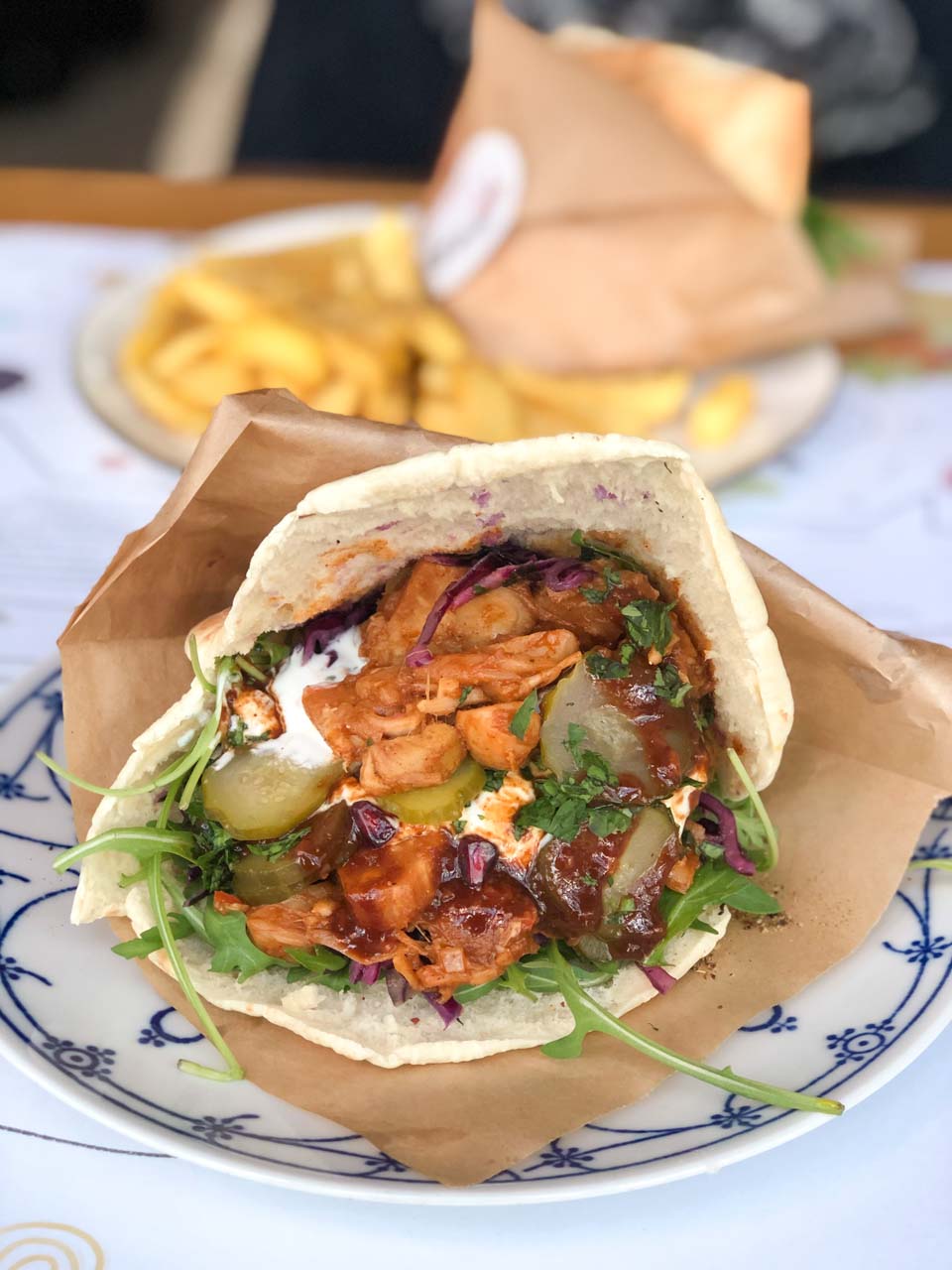 A stuffed flatbread sandwich filled with pulled jackfruit, pickles, greens, and sauces on a patterned plate at Nie/Mięsny in Gdańsk