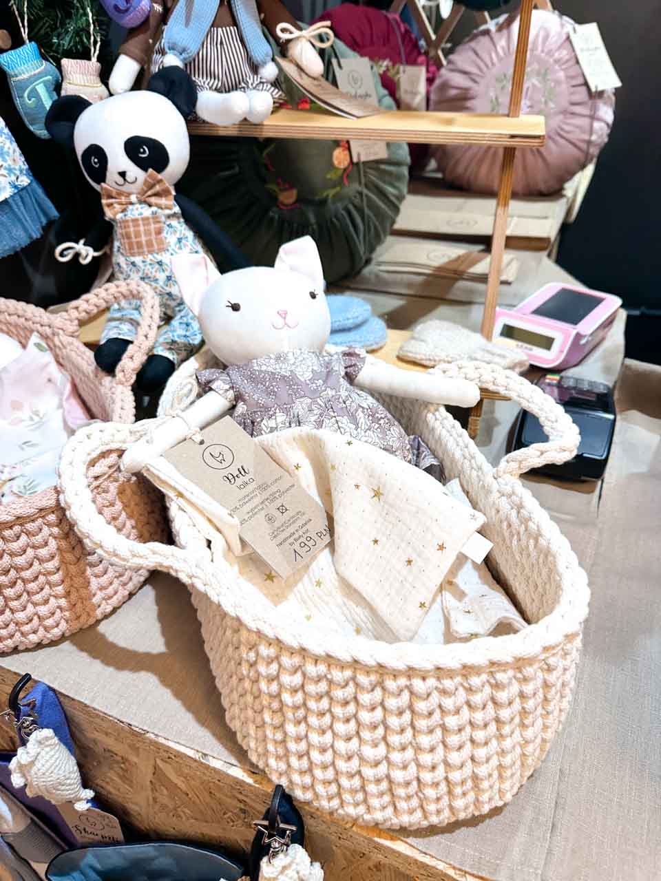 A display of handmade plush toys, including a white cat and a panda, inside crocheted baskets at a Christmas market stall in Gdańsk