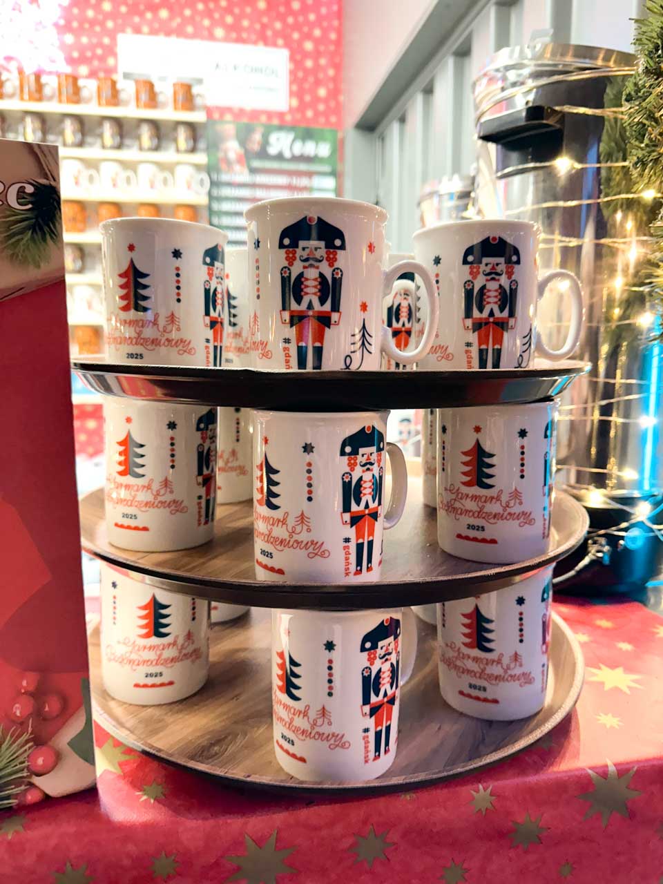 Rows of festive Gdańsk Christmas Market 2025 mugs decorated with nutcracker and tree motifs on a wooden stand