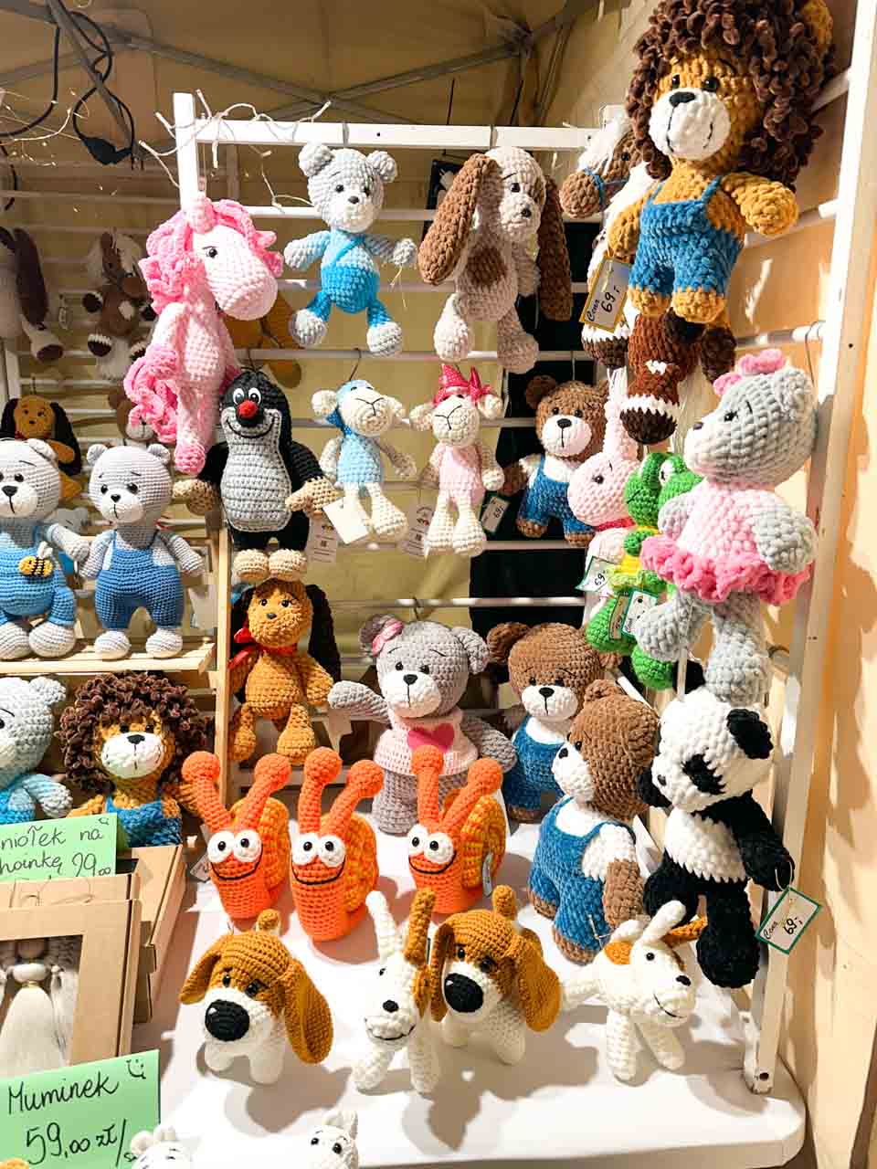 Crocheted stuffed animals including bears, snails, and a unicorn hanging and sitting on white shelves at the Podgórze Christmas Fair of Unique Items in Kraków