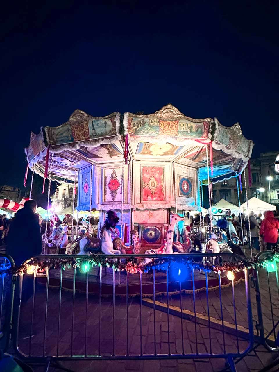 A vintage carousel lit up at night, with children riding festive animals at the Krak&oacute;w Christmas Market in Podg&oacute;rze