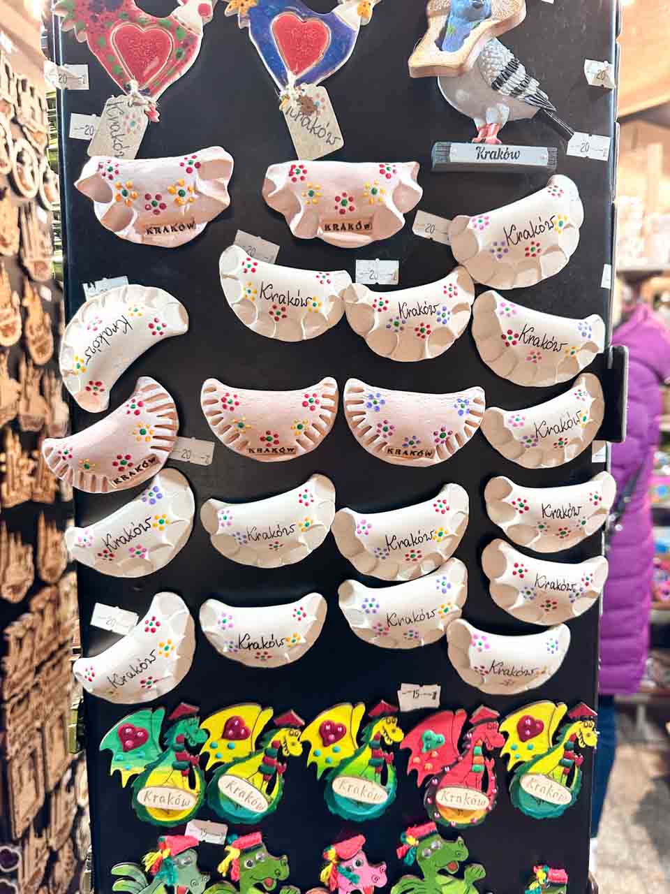 Handmade Krak&oacute;w-themed fridge magnets shaped like pierogi, pigeons, and dragons on a black display