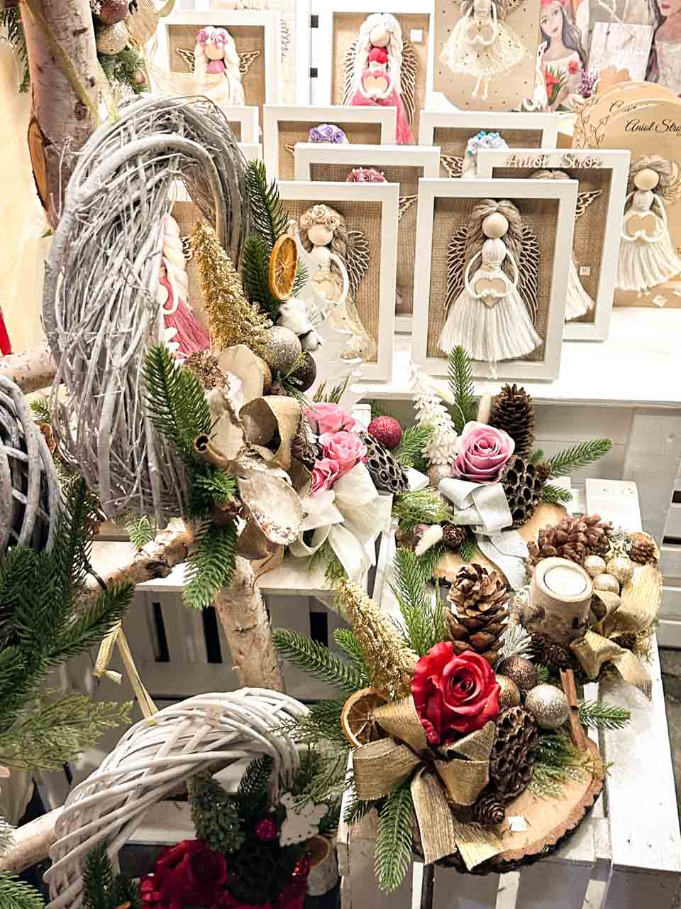 Framed angel decorations and festive wreaths made with pine cones, dried fruit, and ribbon at the Christmas market in Kraków