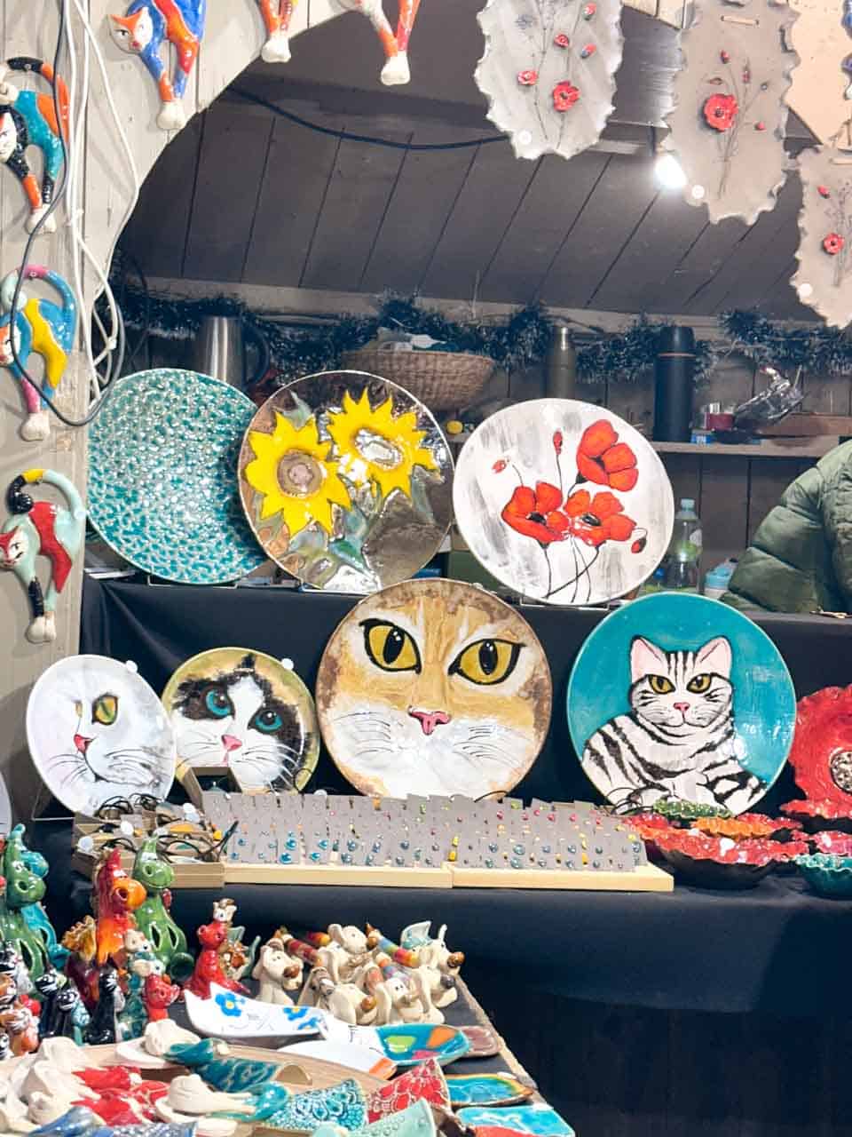 Hand-painted ceramic plates and wall art featuring cats, sunflowers, and red poppies on display at the Christmas market in Krak&oacute;w