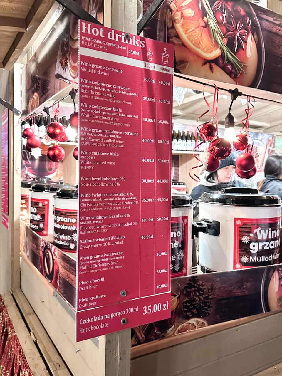 Menu board at a hot drinks stall at the Krak&oacute;w Christmas Market, listing mulled wine and hot beer options with prices in Polish and English