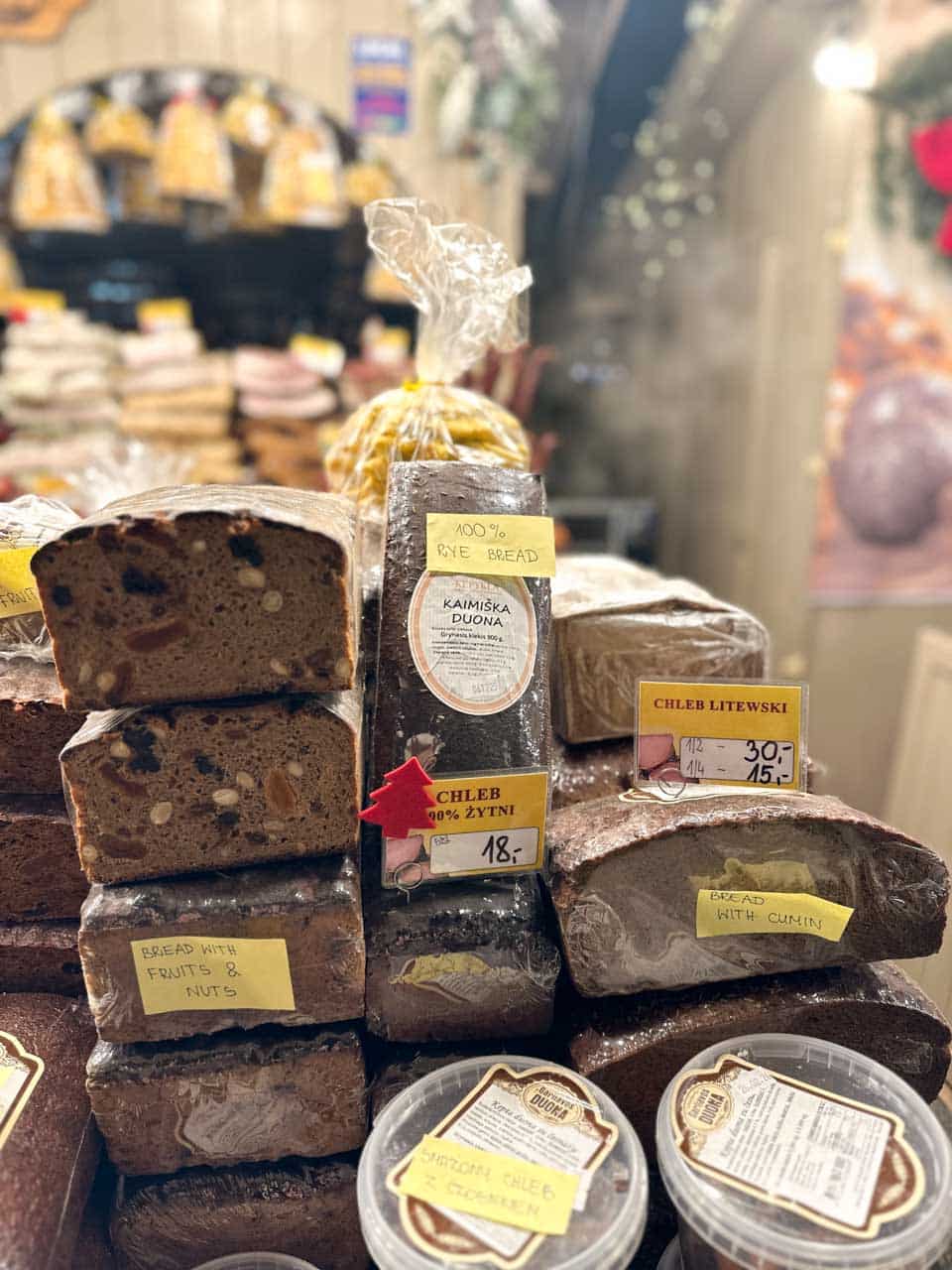 Loaves of rye bread and fruit bread stacked with handwritten price tags at a stall at the Krak&oacute;w Christmas market