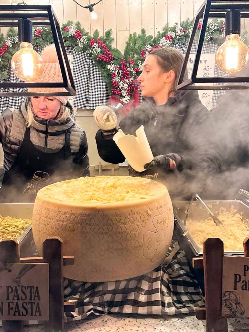 Fresh pasta being tossed inside a giant wheel of cheese at a steaming food stall at the Krak&oacute;w Christmas market