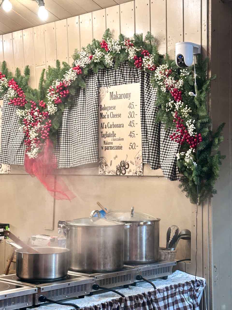 Large pots of pasta cooking behind a festive garland and wooden sign listing the dishes at the Krak&oacute;w Christmas market