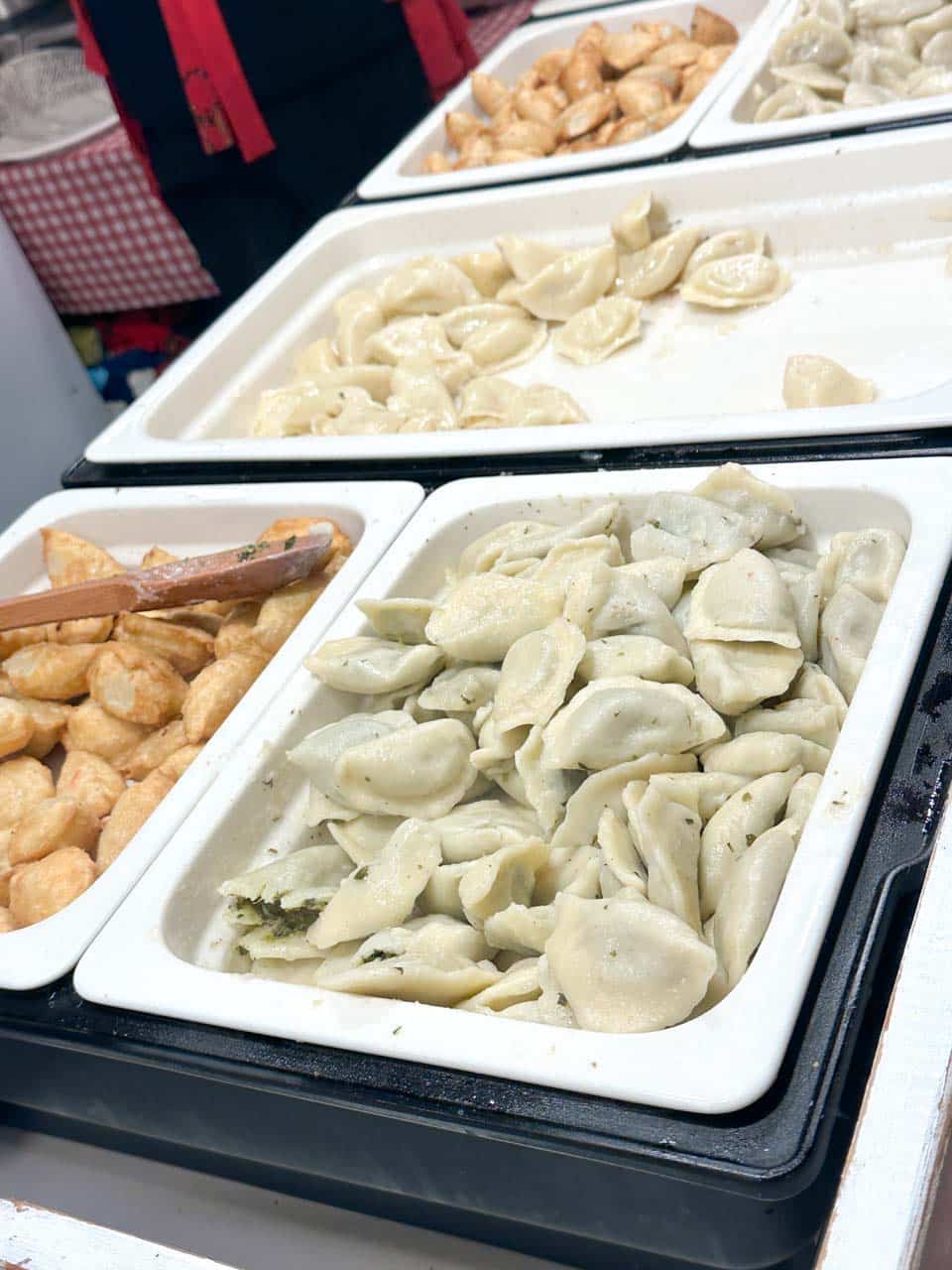 Trays of pierogi at a Christmas market stall in Krak&oacute;w, including spinach, cheese, and fried varieties, ready to be served hot