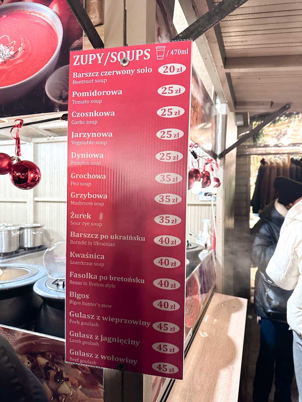 Menu board at a soup stall at the Krak&oacute;w Christmas Market listing beetroot soup, żurek, bigos, and various meat goulashes, with prices