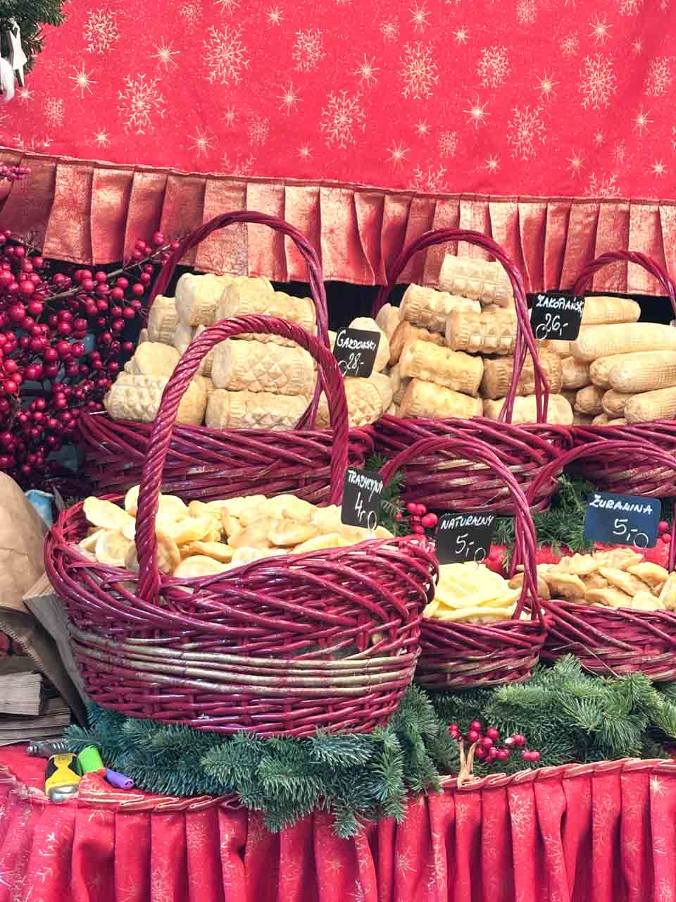 Baskets of traditional oscypek cheese on a stall with red fabric and festive decorations at the Kraków Christmas market