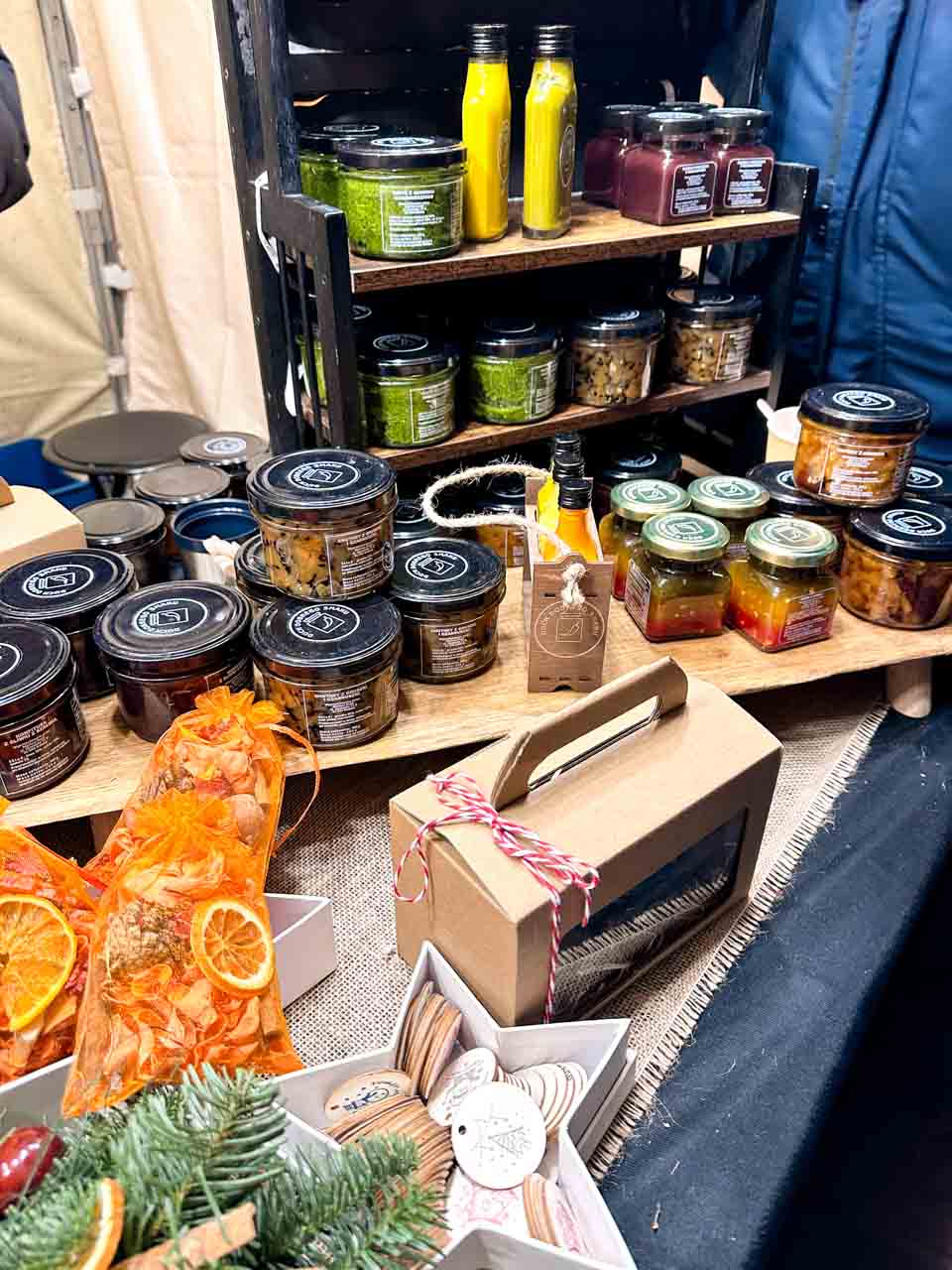 Jars of pesto, pickles, sauces, and preserves stacked on a wooden shelf at a festive food stall in Kraków