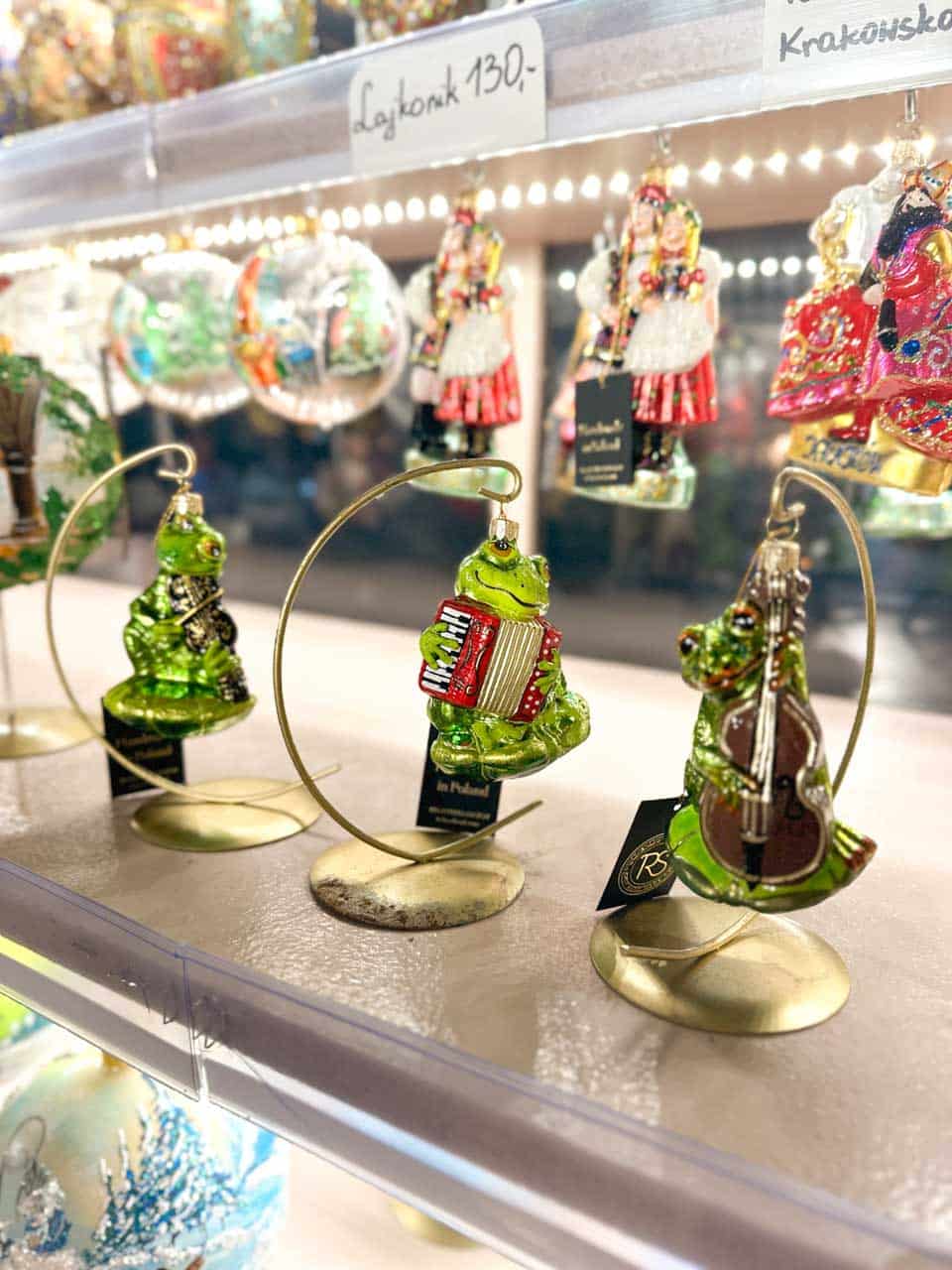 Hand-painted glass ornaments of frogs playing musical instruments, displayed on gold stands at a Christmas decoration stall in Krak&oacute;w, Poland